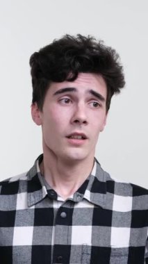 Beyaz arka planda duran kederli beyaz bir gencin portresi. Olumsuz duygu ve kötü akıl sağlığı konsepti. Dikey video.