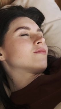 Kafkasyalı mutlu bir kadının yakın portresi. Sabah uyanıp, yatak odasında esniyor. Kameraya bakıp gülümsüyor. Dikey video.