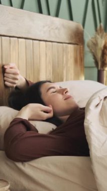 Mutlu beyaz kadın sabahları yatak odasında uyanır. Bayan dinleniyor ve rahat bir yatakta dinleniyor, hafta sonları boş vakit geçiriyor. Dikey video.