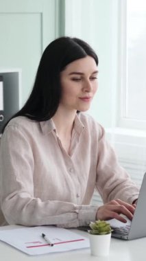 Ofiste çalışan Kafkasyalı mutlu iş kadını dizüstü bilgisayarla mesaj atıyor, iş stratejisi planlıyor. Rahatlamak ve sandalyeye yaslanmak. Dikey video.