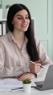 Ofiste çalışırken video görüşmesi yapan ve müşterilerle veya iş arkadaşlarıyla konuşan Kafkasyalı mutlu bir kadın. Çevrimiçi buluşma konsepti. Dikey video.