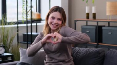 Mutlu, beyaz bir kadının portresi. Aşığın elleri oturma odasında kalp şeklini gösteriyor. Romantik selamlaşma. Sevgililer Günü konsepti.