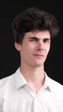 Siyah arka planda gözlerini kapatan iğrenç ve sevimsiz Kafkas genci. Hayal kırıklığı, hayal kırıklığı konsepti. Dikey video.
