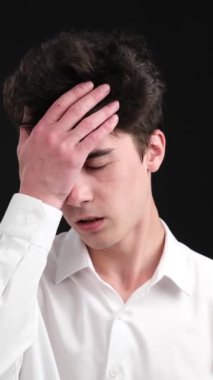 Siyah arka planda facepalm jesti olan hayal kırıklığına uğramış beyaz bir adam. Olumsuz tepki ve duygusal stres konsepti. Dikey video.