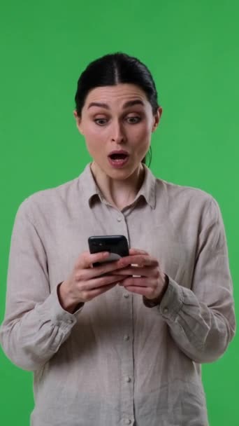 一个惊讶的高加索女人在绿色背景的手机上收到好消息的肖像 在线技术概念 垂直录像 — 图库视频影像