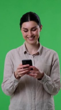 Sosyal medyada mesajlaşan ya da yeşil arka planda cep telefonu kullanan mutlu beyaz kadın. Çevrimiçi eğlence ve iletişim kavramı. Dikey video.