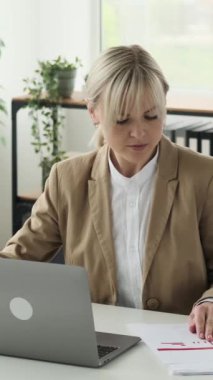 Ofiste evrak ve dizüstü bilgisayarla çalışan Kafkasyalı iş kadını heyecanlı. Planlama ve muhasebe sektörü finansmanı. Dikey video.