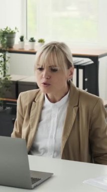 Beyaz kadın çalışanın bilgisayarla görüntülü konuşma yaptığını, ofiste dinlendiğini gösteriyor. Uzaktan iletişim konsepti. Dikey video.