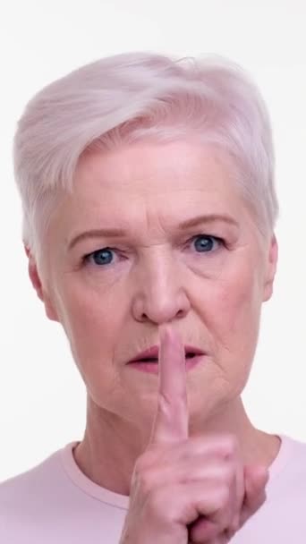 白い背景に秘密や沈黙を保つためのハッシュジェスチャーを示す深刻な高齢の白人女性 プライバシーと秘密の概念 バーティカルビデオ — ストック動画