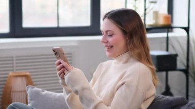 Dost canlısı beyaz bir kadın internette sohbet ediyor ve evinde koltukta telefonla gülüyor. Sosyal medyada boş zamanların ve dinlenmenin keyfini çıkarıyorum..