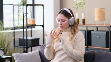 Beyaz, neşeli, müzik dinleyen, kulaklık takan ve evdeki oturma odasında kanepede dans eden genç bir kadın. Hafta sonu rahatlığını kutluyoruz..