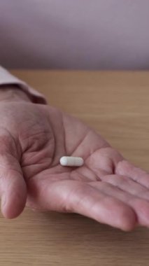 Kafkasyalı yaşlı bir kadının haplı eli yakın çekim. Sağlık, ilaç, koruma, tıbbi terapi konsepti. Dikey video.