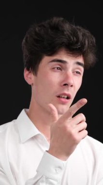 Düşünceli ve ciddi Kafkasyalı genç adam siyah arka plan yerine düşünüyor ya da seçim yapıyor. Hayal gücü, beyin fırtınası konsepti. Dikey video.