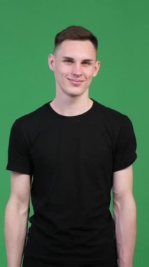 Dost canlısı beyaz adam yeşil arka planda dedikoduları tuttuğu için sessiz jest yapıyor. Sır, sessizlik, gizlilik kavramı. Dikey video.