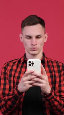 Akıllı telefonlu ciddi bir beyaz adam internette sohbet ediyor ya da kırmızı arka planda internette sörf yapıyor. Sosyal medya ve uzaktan eğlence. Dikey video.