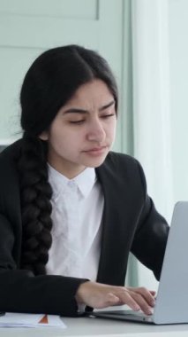 Ofiste dizüstü bilgisayar kullanarak çalışan yorgun Hintli bir kadının portresi. İşten dolayı yorgunluk ve stres, yüksek iş yükü. Dikey video.