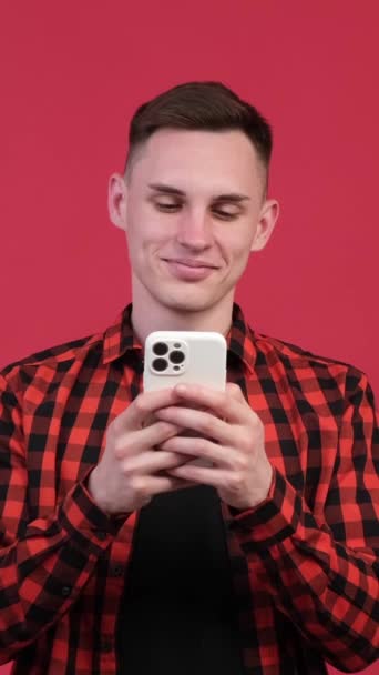 フレンドリーでリラックスした白人男性 学生やビジネスマンの肖像画 携帯電話を持ち 赤い背景でカメラを見ています バーティカルビデオ — ストック動画