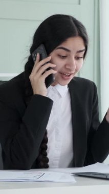 Kızgın Hintli iş kadını ofisteki telefonda agresif bir şekilde konuşuyor. Belgeleri gözden geçirip sorunu çözmeye çalışıyorum. Dikey video.
