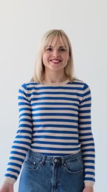 Gülümseyen ve neşeli beyaz kadın şakacı bir şekilde hava öpücüğü veriyor ve beyaz arka planda flört ediyor. Tutku, sevgi. Dikey video.