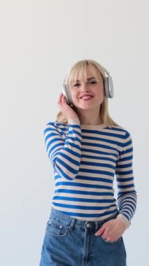 Beyaz arka planda kablosuz kulaklıkla müzik dinleyen neşeli beyaz bir kadının portresi. Keyif ve rahatlama konsepti. Dikey video.