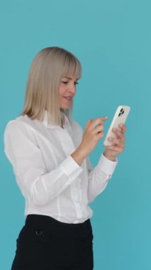 Beyaz kadının internette iyi haberler almasına şaşırdım. Mavi arka planda akıllı telefonuyla kutlama yapıyor ve haykırıyor. Dikey video.