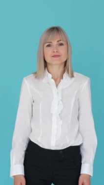 Mavi arka planda kollarını açıp omuz silken neşeli beyaz kadın. Soru, merak, yanlış anlaşılma. Dikey video.