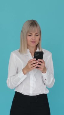 Şaşırmış Kafkas kadın ofis çalışanı, çevrimiçi çalışıyor, cep telefonu kullanıyor ve başarıyı kutluyor ya da mavi arka planda iyi haberler.