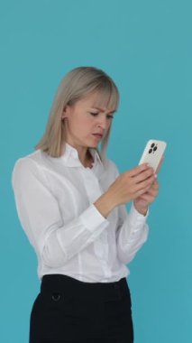 Öfkeli Kafkasyalı kadın telefonla çalışıyor, mavi arka planda duruyor. İşle ilgili sorunlar, duygusal stres kavramı. Dikey video.