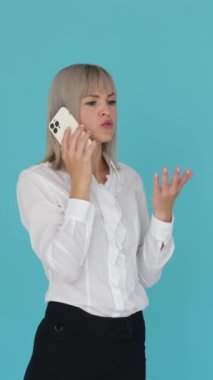 Mutlu ve pozitif beyaz kadın mavi arka planda telefonla konuşuyor. Uzaktan konuşma ve müzakere konsepti. Dikey video.