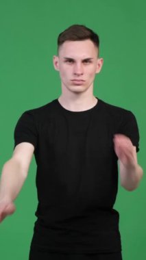 Stern Kafkasyalı genç adam yeşil arka planda anlaşmazlık içinde çapraz kollarla dur işareti gösteriyor. Kısıtlama, reddetme, reddetme. Dikey video.