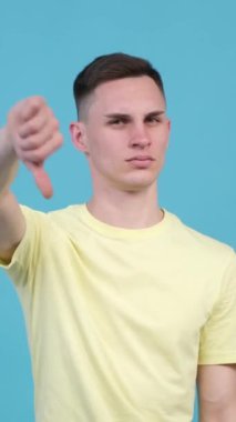 Mavi arka planda başparmağını gösteren ya da hoşlanmayan beyaz bir adamın portresi. Reddedilme, içki yasağı. Dikey video.
