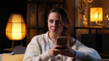 Akşamları internette akıllı telefonuyla internetten sohbet eden heyecanlı bir beyaz kadın. Uzak iletişim siber uzayı kavramı.