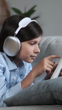 Neşeli beyaz öğrenci evdeki kanepede dinleniyor ve internet aktiviteleri ve online eğlence için telefon kullanıyor. Dikey video.
