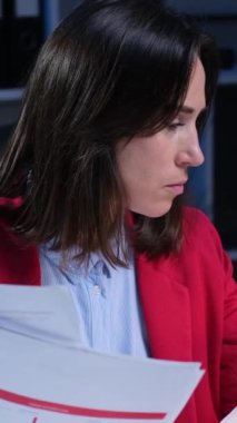 Kafası karışmış, evrak işleriyle uğraşan, akşam ofisinde çalışırken omuz silken omuz silken beyaz kadın çalışan. Dikey video.
