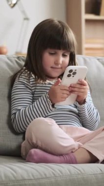 Mutlu Kafkasyalı anaokulu kızı cep telefonunu online eğlence ya da internet gezisi için kullanıyor. Ev içi boş zaman konsepti. Dikey video.