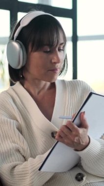 Neşeli, beyaz, genç, yetişkin bir kadın evdeki deftere düşüncelerini ve düşüncelerini yazıyor. Alışveriş listesi, ajanda ya da program oluşturuluyor. Dikey video.