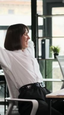 Kafkasyalı orta yaşlı iş kadını koltuğa yaslanıyor, iş gününün bitişini kutluyor ve ofisten ayrılıyor. Dikey video.