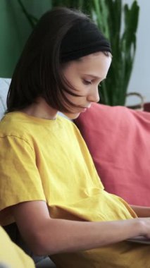 Ciddi bir beyaz çocuk ev oturma odasında online eğlence için dizüstü bilgisayar kullanıyor. Dinlenmek ve boş zaman geçirmek. Dikey video.