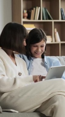 Neşeli Kafkas anne ve genç oğlu boş zamanlarını evde kanepede oturup tablet bilgisayar kullanarak geçiriyorlar. Dikey video.