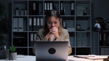 Akşam ofisinde dizüstü bilgisayarla çalışan sinirli, beyaz, genç bir ofis çalışanı. İş baskısı ve gerilim kavramı, zorluklar.