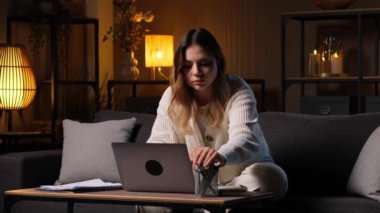 Odaklanmış beyaz kadın ofis çalışanı not defterine not alıyor, akşam evde dizüstü bilgisayarla çalışıyor. Muhasebe işi ya da başlangıç.