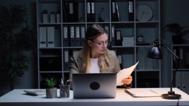 Laptop ve evraklarla çalışan beyaz, genç, yetişkin bir iş kadını. Bütçe ve mali denetim.