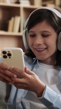 Kafkasyalı genç bir öğrenci akıllı telefonuyla vakit geçirip evde gülüyor. Çevrimiçi eğlence ve internet sosyal medya kavramı. Dikey video.