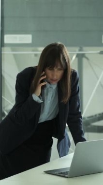 Odaklanmış Kafkasyalı orta yaşlı serbest çalışan kadın ofiste telefonla konuşuyor. İş görüşmeleri kavramı. Dikey video.