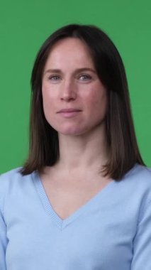 Neşeli ve kendinden emin orta yaşlı beyaz bir kadının portresi, yeşil arka planda kameraya bakan pozitif bir kadın. Dikey video.