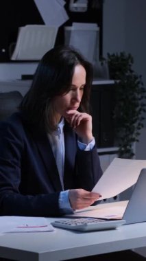 Akşam ofisindeki belgelerle uğraşırken, düşünceli beyaz kadın serbest yazar proje ya da strateji geliştiriyor. Dikey video.