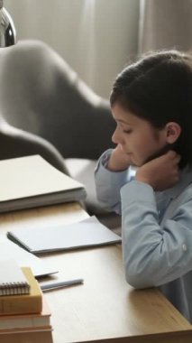 Odaklanmış beyaz çocuk okul ödevlerini yapıyor, deftere yazıyor, evde oturuyor. Uzak öğrenim kavramı. Dikey video.