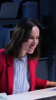 Kafkasyalı neşeli kadın çalışanın elinde para var ve gece geç saatlerde ofiste çalışırken mali zenginliği kutluyorlar. Dikey video.