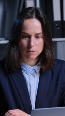 Ciddi bir orta yaşlı Kafkasyalı ofis çalışanı akşam ofisindeki dizüstü bilgisayarla iş muhasebe ve teftiş bilgilerini inceliyor. Dikey video.