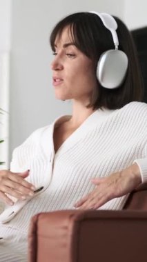 Beyaz bir kadın, evdeki video görüşmesi için laptopunu kullanarak koltukta dinleniyor. Arkadaşlarla neşeli bir sohbet. Dikey video.